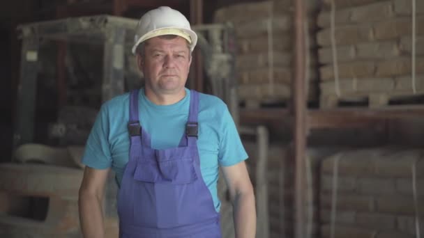 Porträtt av allvarlig vit man i blå uniform och vit hjälm poserar på fabrik eller fabrik. Självsäker man anställd korsa händer och titta på kameran som stående på lager. — Stockvideo