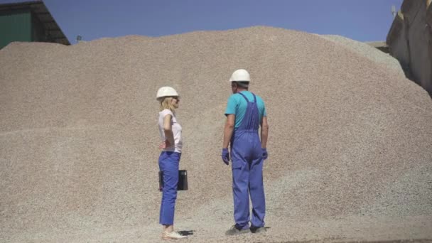 Weite Aufnahmen von Fabrikarbeitern, die im Freien vor einem riesigen Steinhaufen stehen. Mitarbeiter eines kaukasischen Werks erhält an einem sonnigen Sommertag Material von einem Auftragnehmer. — Stockvideo