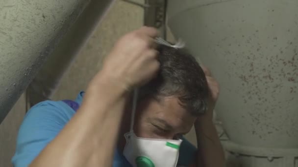 Close-up face of serious factory worker putting on protective face mask and safety helmet at factory. Professional Caucasian man working at manufacturing site indoors with dangerous materials. — Stock Video