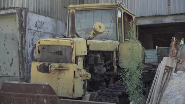 Beschädigter rostiger Traktor steht auf verlassenen Fabrikruinen. Vernachlässigte zerstörte Maschinen im Freien. Altes Industriegebäude und kaputter Transport. — Stockvideo