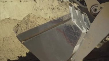 Açık hava fabrikasında içi sarı kum dolu bir traktör. Güneşli yaz gününde fabrikada çalışan endüstriyel makineler. Beton imalatı için malzeme yükleme.