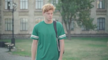 Mutsuz kızıl saçlı genç adam kampüste gülen grup arkadaşlarının yanından geçiyor. Alay edilmekten muzdarip beyaz üniversite öğrencisinin portresi. Zorbalık ve eğitim kavramı.