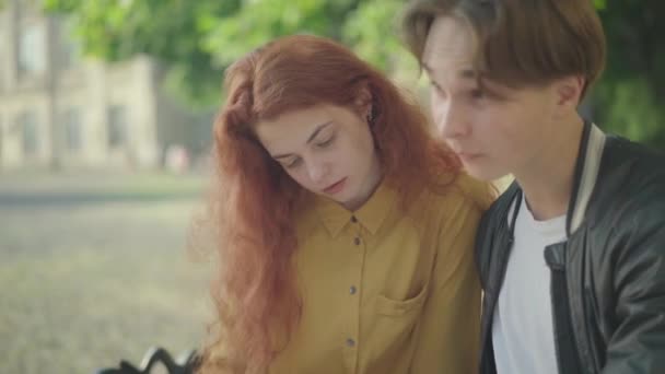 年轻迷人的白种人红头发女人和男人坐在户外聊天的画像。积极的大学生在大学校园里学习后休息。休闲概念. — 图库视频影像