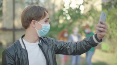 Genç esmer beyaz adamın portresi akıllı telefonda kablosuz sohbet kullanıyor. Yurtdışında Covid-19 salgını üzerine çalışan neşeli bir üniversite öğrencisi. Coronavirus yaşam tarzı ve eğitimi.