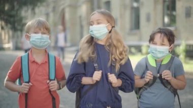 Arka planda bulanık lise öğrencileri gibi poz veren yüz maskeli beyaz öğrenciler var. Covid-19 pandemik karantina üzerine çalışan sevimli çocukların portresi.