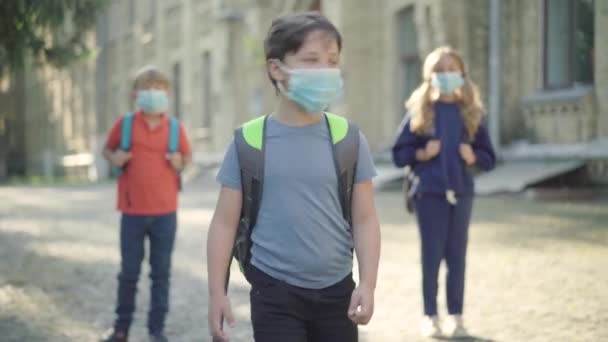 Estudiantes de secundaria con máscaras faciales divirtiéndose en el patio de la escuela en un día soleado. Retrato de las pupilas caucásicas positivas relajadas huyendo. Niños disfrutando del ocio después de estudiar en la pandemia de Covid-19. — Vídeos de Stock