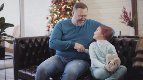 긍정적 인 아버지가 크리스마스 이브에 어린 딸에게 키스하고 여자 머리를 빗고 있습니다. 행복 한 남자와 아이가 집에서 새해를 보내는 모습. 기쁨과 축하의 개념. — 비디오