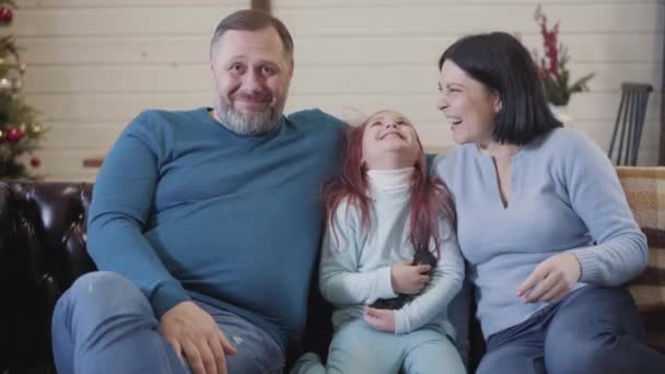 Carefree família caucasiana amigável assistindo filme de comédia na TV em casa. Visão frontal retrato de homem, mulher, e menina alegre mid-adulto sentado no sofá e rindo. — Vídeo de Stock