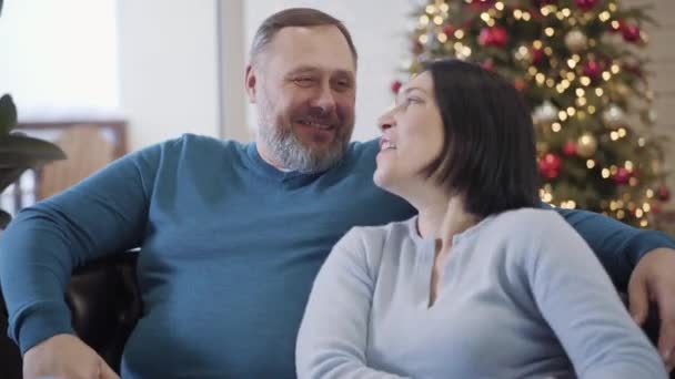 Κοντινό πλάνο πορτραίτο του θετικού Καυκάσου άνδρα και γυναίκα που μιλάει και γελάει με το δέντρο της Πρωτοχρονιάς στο παρασκήνιο. Χαλαροί σύζυγοι που διασκεδάζουν την παραμονή των Χριστουγέννων στο σπίτι. — Αρχείο Βίντεο