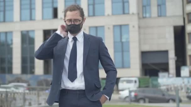 Retrato de un hombre de negocios caucásico cansado con anteojos y mascarilla de pie en la calle urbana de la ciudad y el cuello frotado. Joven hombre exitoso agotado por el estrés empresarial en la pandemia de Covid-19. — Vídeos de Stock