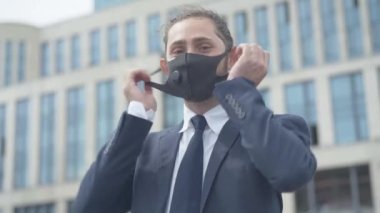 Yüzündeki maskeyi çıkarıp zafer jesti yapan gülümseyen beyaz adamın portresi. Yakışıklı, kendinden emin iş adamı Covid-19 salgınının sona ermesine seviniyor. Coronavirus konsepti.