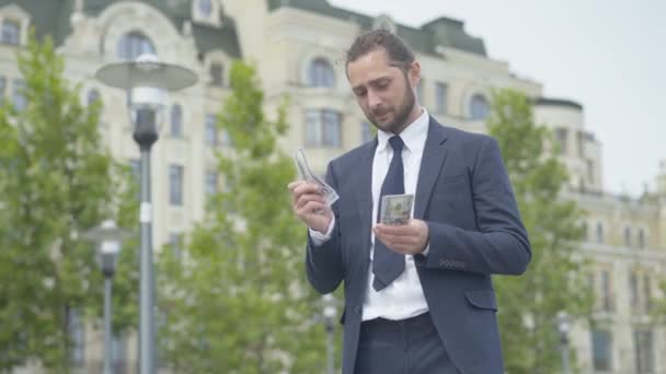 Confiado exitoso empresario rico contando dólares y sonriendo. Retrato de un joven caucásico feliz con dinero al aire libre en la ciudad urbana. Concepto de riqueza y éxito. — Vídeo de stock