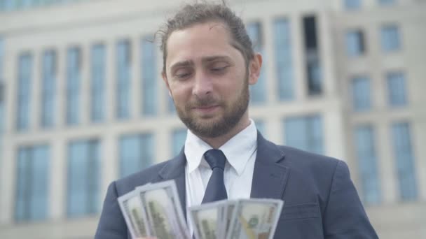 Portret przystojnego biznesmena liczącego pieniądze na zewnątrz. Szczęśliwy, pewny siebie biały mężczyzna, patrzący na paczkę dolarów i uśmiechający się. Bogactwo i sukces. — Wideo stockowe