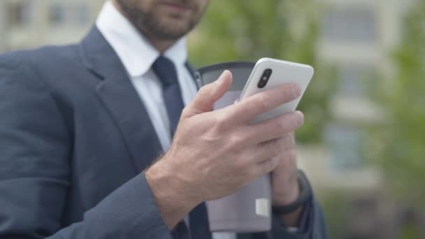 De cerca mano de irreconocible hombre de negocios caucásico navegar por Internet o mensajería en línea utilizando el teléfono inteligente. Hombre seguro de éxito comprobando el correo electrónico al aire libre en la calle de la ciudad. — Vídeos de Stock