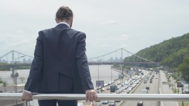 Back view of desperate depressed Caucasian man standing at bridge fence ready to jump down on urban highway. Middle shot of frustrated businessman trying to solve problems with suicide. — Stock Video