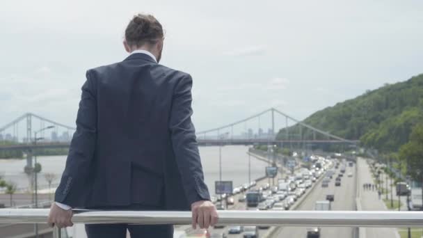 Vue arrière de l'homme caucasien désespéré déprimé debout à la clôture du pont prêt à sauter sur l'autoroute urbaine. Plan médian d'un homme d'affaires frustré essayant de résoudre des problèmes de suicide. — Video