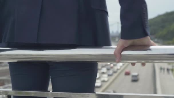 Primer plano de la mano caucásica masculina sosteniendo la cerca del puente. Joven hombre de negocios irreconocible parado en el borde listo para suicidarse saltando abajo en la carretera urbana. — Vídeos de Stock
