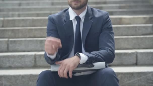 Неузнаваемый бизнесмен снимает очки и вздыхает. Молодой кавказский стресс мужчина сидит на городской лестнице и думает. Перегруженный работой предприниматель в официальном иске. — стоковое видео