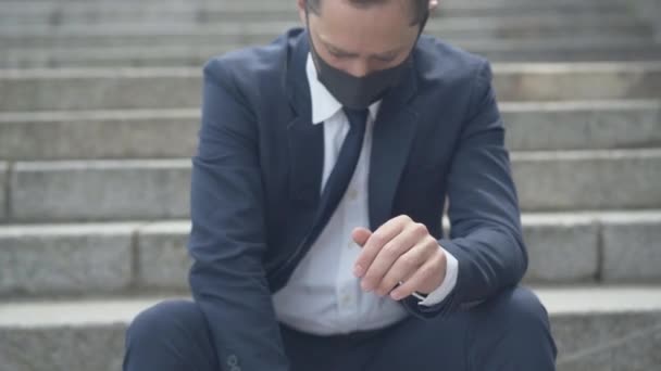 Unrecognizable young Caucasian man raising attache case. Tired businessman in Covid-19 face mask sitting on urban city stairs during coronavirus pandemic and sighing. Tiredness and stress concept. — Stock Video