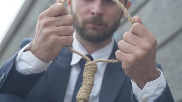 Primer plano de las manos caucásicas masculinas sosteniendo la cuerda con un joven borroso pensando en el fondo. Un desesperado hombre de negocios frustrado preparando el suicidio. Concepto de estrés y depresión. — Vídeos de Stock