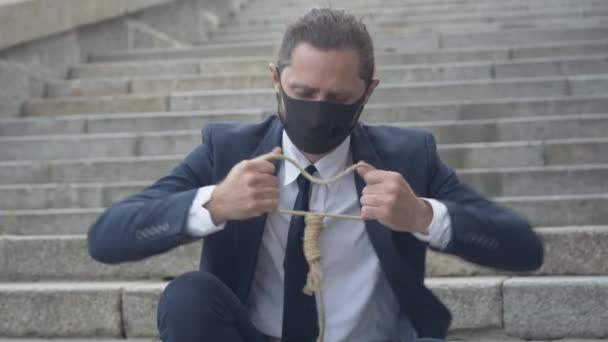 Porträt eines frustrierten Geschäftsmannes mit Covid-19-Gesichtsmaske bei der Überprüfung eines selbstmörderischen Seils. Junger depressiver Mann aus dem Kaukasus versucht Selbstmord zu begehen. Auswirkungen des Coronavirus. — Stockvideo