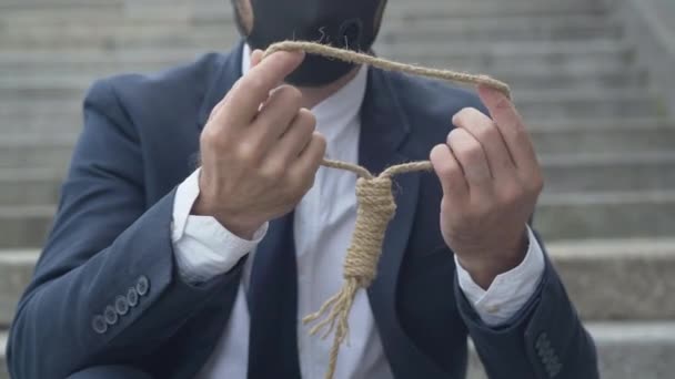 Неузнаваемый белый мужчина в маске Ковида-19 проверяет силу веревки для самоубийства. Молодой отчаянный бизнесмен подумывает повеситься. — стоковое видео
