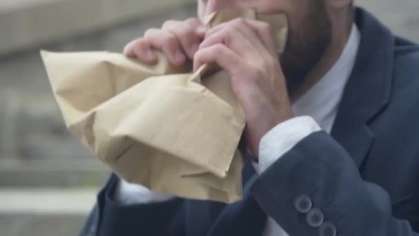 Gros plan d'un homme nerveux frustré essayant de se calmer en respirant dans un sac en papier. Stressé homme d'affaires caucasien ayant crise d'anxiété à l'extérieur assis sur les escaliers de la ville urbaine. Stress et surmenage. — Video
