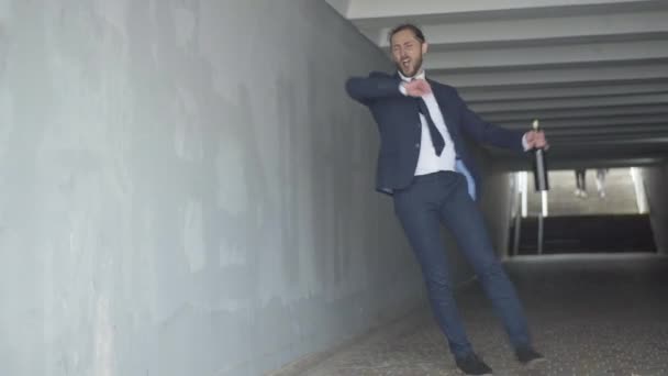 Amplio retrato de un hombre de negocios caucásico borracho caminando con una botella de vino a lo largo del cruce subterráneo. Hombre guapo en traje formal celebrando acuerdo de negocios exitoso o chico deprimido perdió su trabajo. — Vídeos de Stock