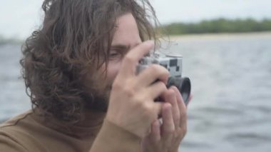 Doğanın fotoğraflarını çekmek için retro kamera kullanan mutlu beyaz adamın yakın plan yüzü. Açık havada eğlenen gülümseyen erkek fotoğrafçının portresi. Yaşam tarzı ve mutluluk.