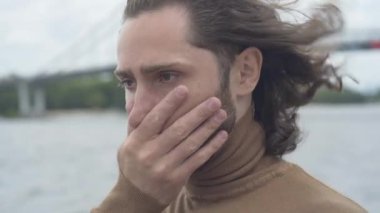 Rüzgarlı bir günde dışarıda dikilen yaralı gözlü sinirli genç adamın yakın plan yüzü. Kasvetli bir günde, nehir kıyısındaki umutsuz beyaz adamın portresi..