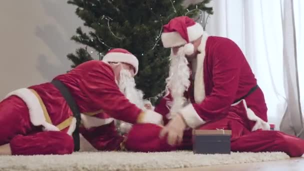 Dos Santa Claus en trajes rojos luchando por la bolsa de Navidad en el interior. Hombres caucásicos sacando regalos. Concepto de celebración de Año Nuevo. — Vídeo de stock