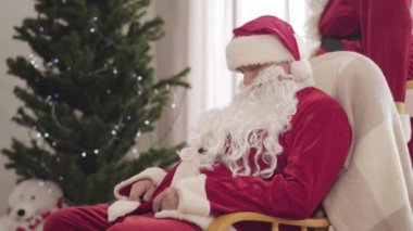 Kırmızı Noel kostümlü yaşlı adam sallanan sandalyede uyuyan genç Noel Baba ile odaya giriyor. Adam yılbaşı arifesinde meslektaşını uyandırıyor..