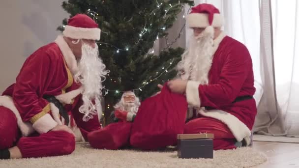 산타 할아버지가 조항에서 선물 가방을 훔치고 있어. 빨간 크리스마스 의상을 입은 두 남자가 선물 가방을 당기고 있습니다. 새해 휴일. — 비디오