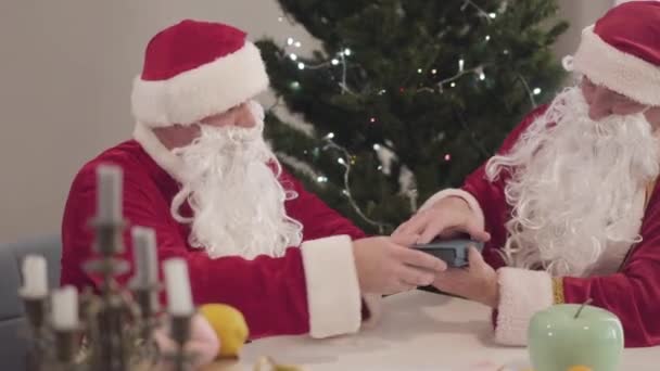 Santa giving present to colleague on New Years eve. Caucasian man in red costume and false beard giving car keys in gift box for senior Santa Clause. Christmas celebration. — Stock Video