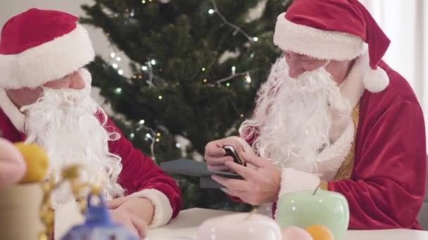 İki Noel Baba el sıkışıyor ve konuşuyor. Kırmızı kostümlü kıdemli adam arabanın anahtarlarını tutuyor ve hediye için meslektaşına teşekkür ediyor. Yeni yıl ve Noel konsepti. — Stok video