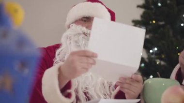 Genç ve yaşlı Noel Babalar Noel arifesinde mektupları inceliyor. Kırmızı Noel kostümlü iki adamın portresi yeni yıl tatilinde dilekleri okuyor..