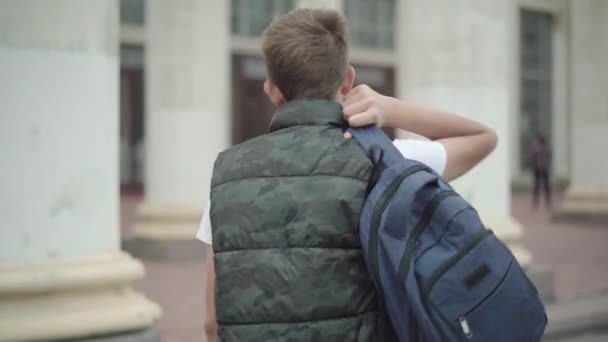 Вид на кавказского школьника с рюкзаком, идущего к школьному зданию. Брюнетка идет на учебу. Концепция образования и обучения. — стоковое видео