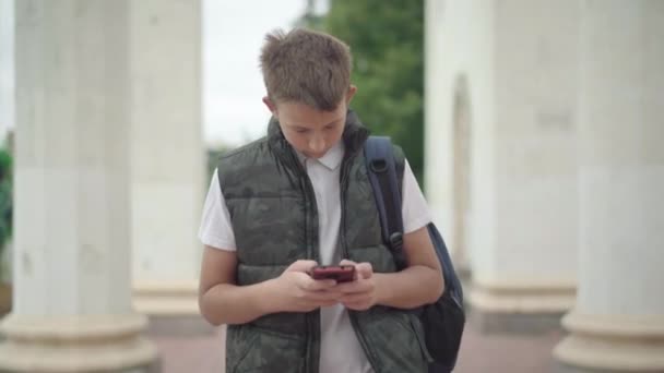 Absorbierter kaukasischer Junge, der mit Rucksack und Smartphone läuft. Porträt eines vertieften Schülers, der im Internet surft oder Nachrichten verschickt. Geräteabhängigkeit der Generation Z. — Stockvideo