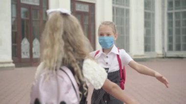 Covid-19 maskeli iki liseli kız dışarıda sarılıyor. Coronavirus salgını sırasında okul tatilinden sonra toplanan mutlu beyaz kızların portresi.