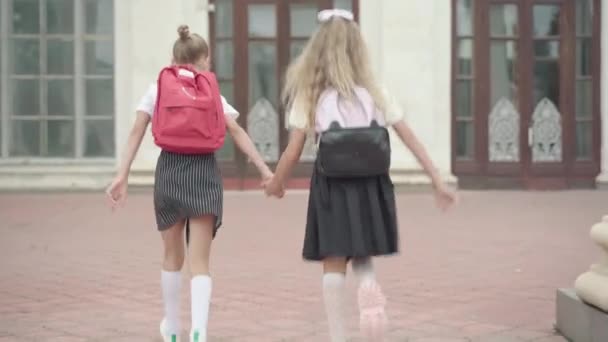 Back view of cheerful girls running to school in the morning. Wide shot of happy Caucasian schoolgirls going to studying outdoors. Happy education and childhood. — Stock Video