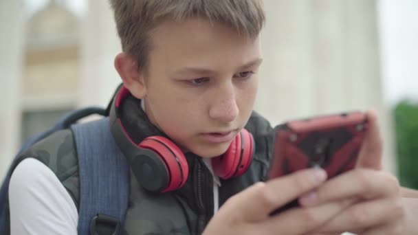 Зблизька концентрований хлопчик користується соціальними медіа на смартфоні. Портрет поглиблених кавказьких шкільних повідомлень онлайн після навчання. Покоління Z спосіб життя і залежність від пристроїв. — стокове відео