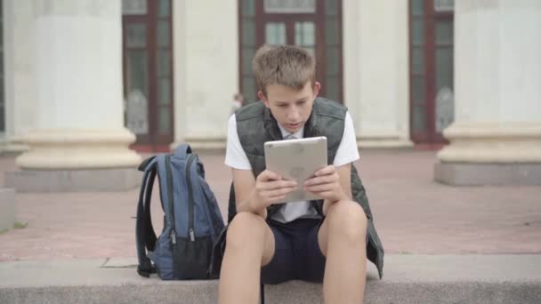 Portrait d'un écolier caucasien fatigué utilisant une tablette pendant les vacances scolaires à l'extérieur. Sleepy boy surfer sur Internet ou messagerie en ligne. Mode de vie de la génération Z. — Video