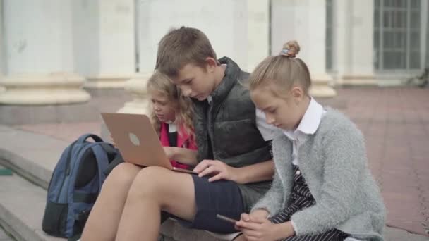 Widok boczny pokolenia Z dzieci surfujących po Internecie na urządzeniach w przerwie szkolnej. Wchłonął uczniów korzystających z mediów społecznościowych na smartfonie, laptopie i tablecie. — Wideo stockowe