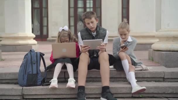 Die Kamera nähert sich Kindern mit Hilfe von Geräten und Blicken auf die Kamera. Porträt der Generation Z: Junge und Mädchen surfen während der Schulpause im Internet. — Stockvideo
