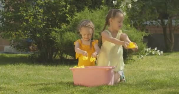 Ampla foto de irmãs caucasianas felizes brincando com brinquedos de patinho no dia ensolarado de verão ao ar livre. Meninas bonitas desfrutando de lazer. Infância e relaxamento. Cinema 4k ProRes HQ. — Vídeo de Stock