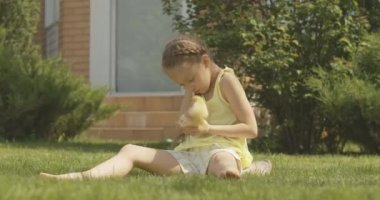 Açık havada ördek yavrusuyla oynayan neşeli beyaz kızın geniş açılı portresi. Evcil kuşla yaz tatilinin tadını çıkaran sevimli bir çocuk. Sinema 4k ProRes Merkezi.