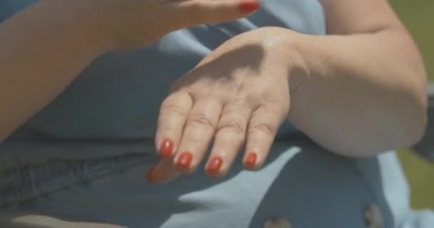 Primo piano di mani curate femminili più anziane che applicano la crema idratante. Donna caucasica irriconoscibile che si prende cura della pelle all'aperto nella soleggiata giornata estiva. Cinema 4k ProRes HQ. — Video Stock