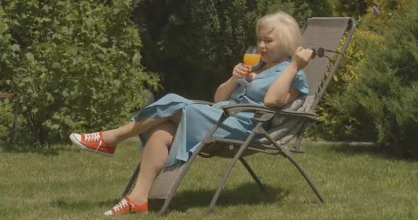 Yazlık bahçede portakal suyu içen Kafkasyalı kadın emeklilerin yan görüntüsü. Mutlu gülümseyen kadının açık havada güneşli bir emeklilik gününün geniş açılı portresi. Sinema 4k ProRes Merkezi. — Stok video