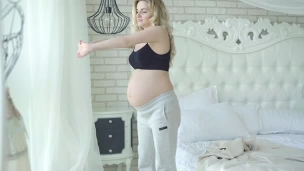 Atletisk gravid kvinna som står upp från sängen och stretchar. Porträtt av leende kaukasiska förväntansfulla träning på morgonen hemma. Friska livsstil och graviditet koncept. — Stockvideo