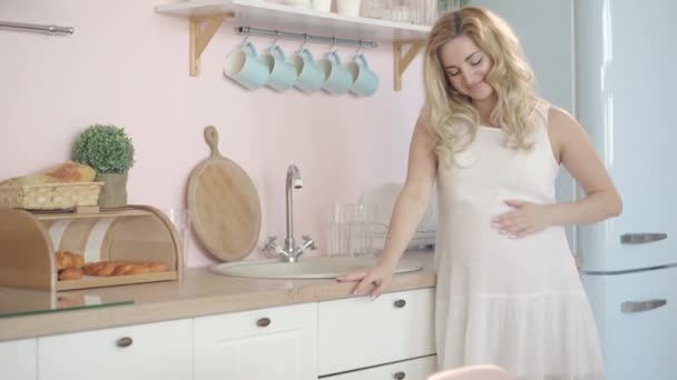 摄像机靠近快乐的孕妇，她站在厨房里抚摸着肚子。轻松自在、自信的高加索女人在家中享受怀孕的画像. — 图库视频影像